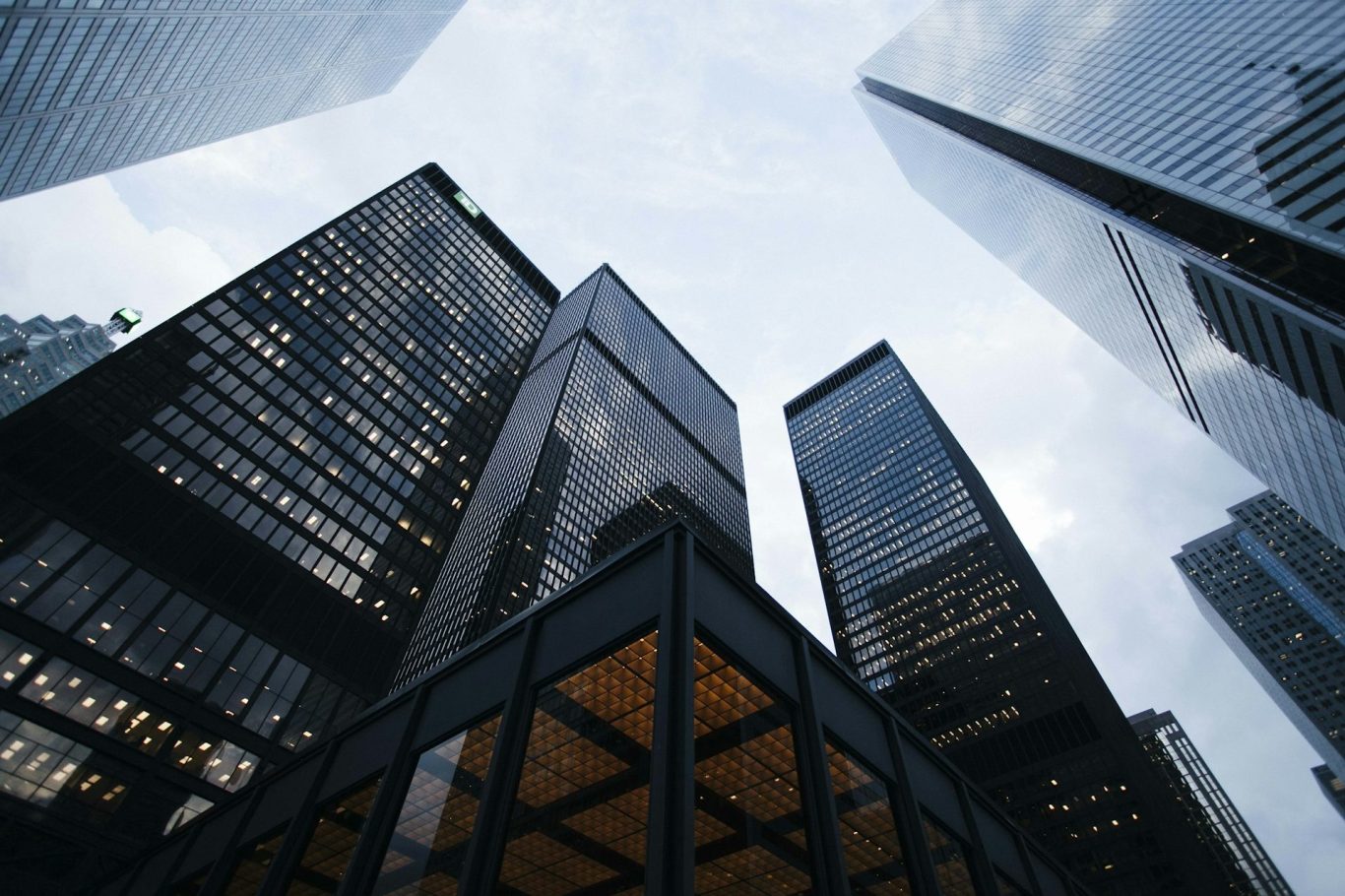 Skyscrapers in a financial district near San Francisco reach toward a cloudy sky, viewed from ground level.